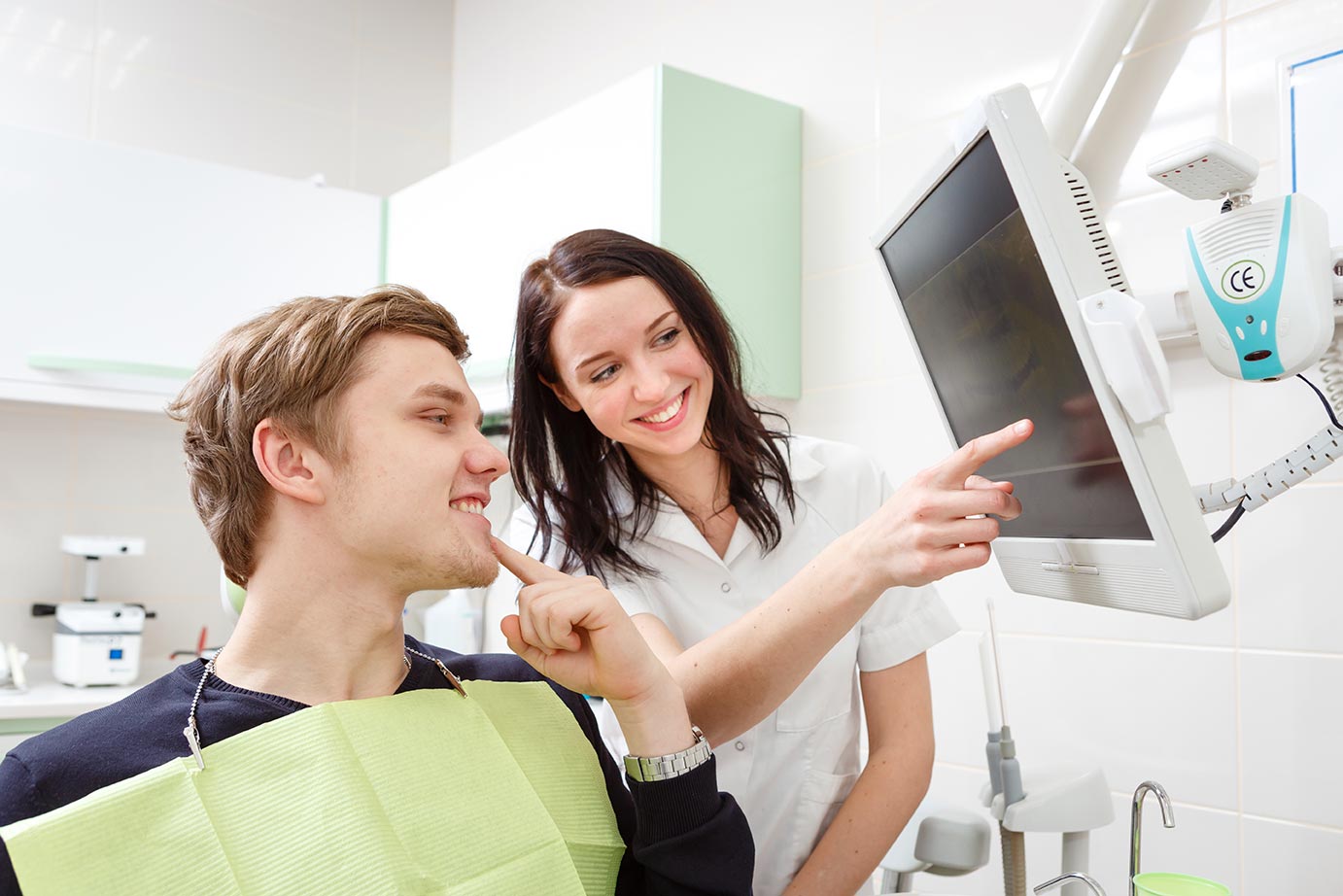 A dental hygienist reviews a dental scan with her patient, a young man in a blue shirt.
