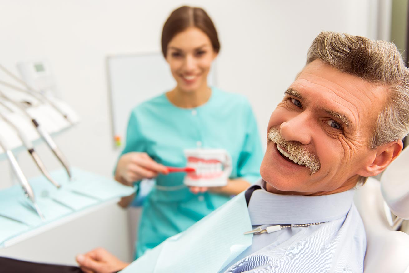A dental patient with a mustache and white hair smiles for a photo while sitting in the patient's chair.